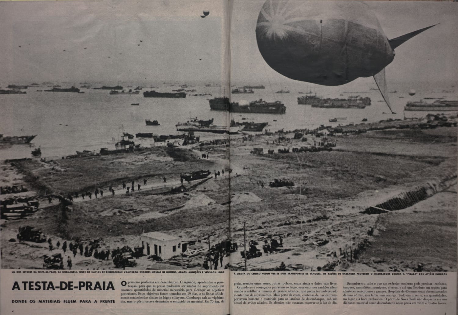 Fotografia panorâmica da praia da Normandia durante o desembarque aliado, com navios, tropas, veículos e balão de barragem visíveis.